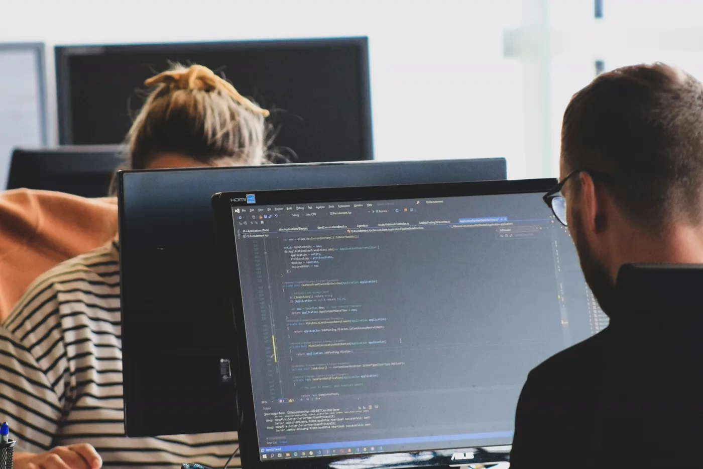 Two developers reviewing code together on dual monitors in a modern engineering office