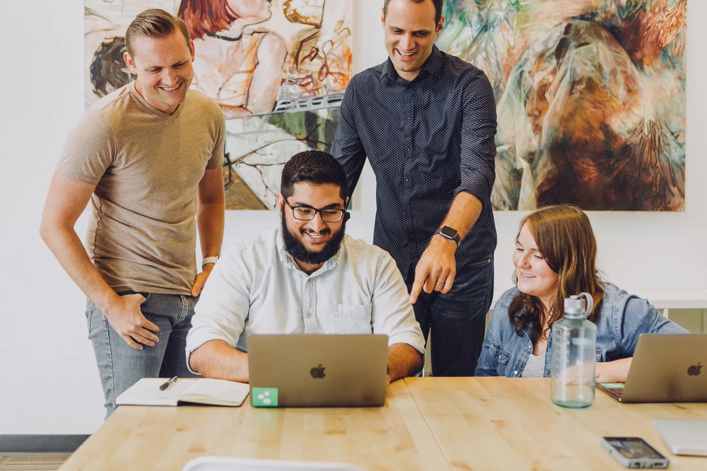 Product team smiling around a laptop reviewing progress in a bright office