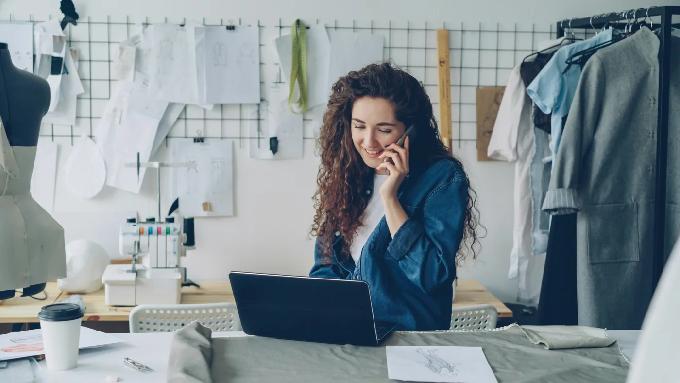 Fashion designer on the phone reviewing storefront UX on a laptop