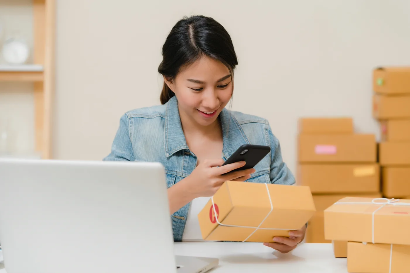 Merchant reviewing her live Shopify store on a laptop, smiling beside packed order boxes